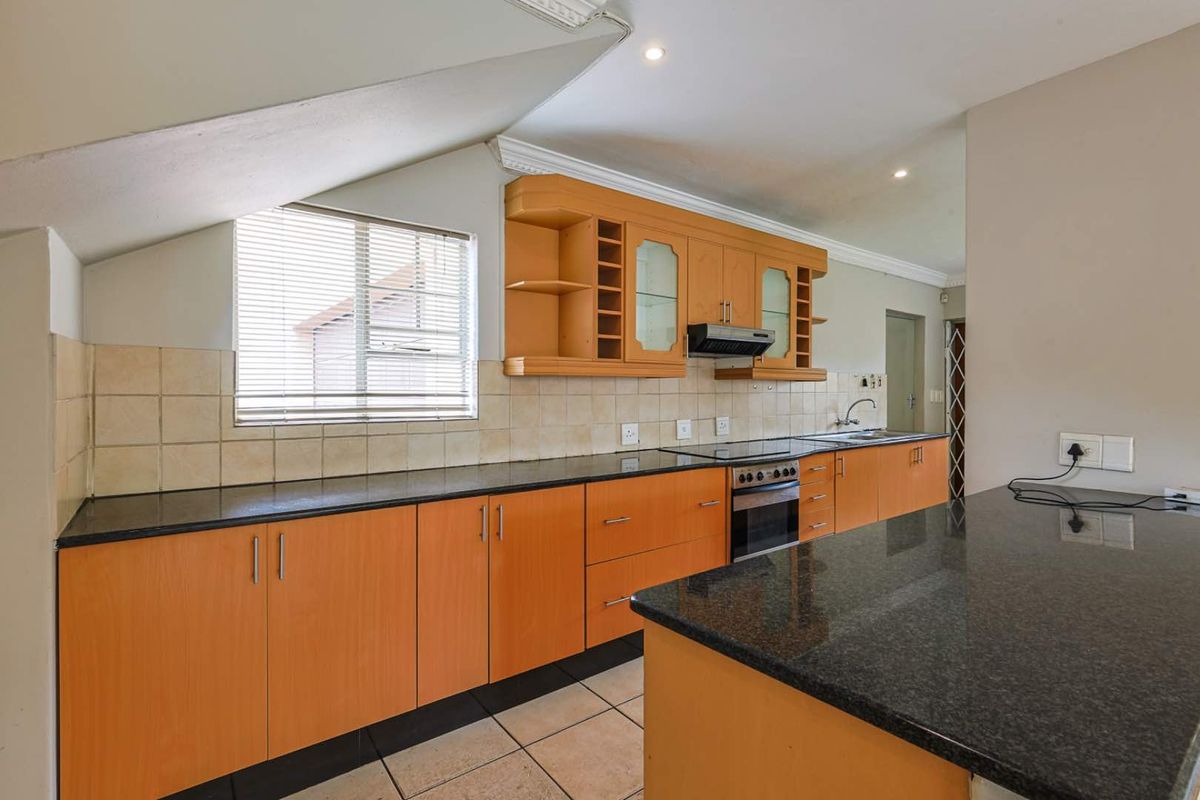 A functional kitchen featuring wooden cabinetry, dark granite countertops, a built-in oven with extractor fan, and tiled flooring under a sloped ceiling.