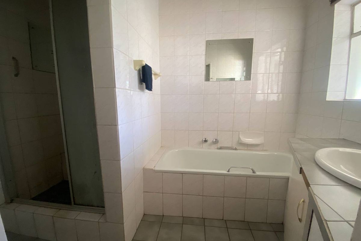 A functional bathroom featuring a built-in bathtub, separate shower enclosure, and a vanity basin with tiled wall and floor finishes.