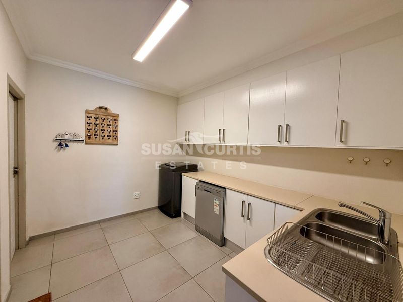 A functional laundry room featuring white built-in cabinetry, a double bowl sink with mixer tap, and tiled flooring.