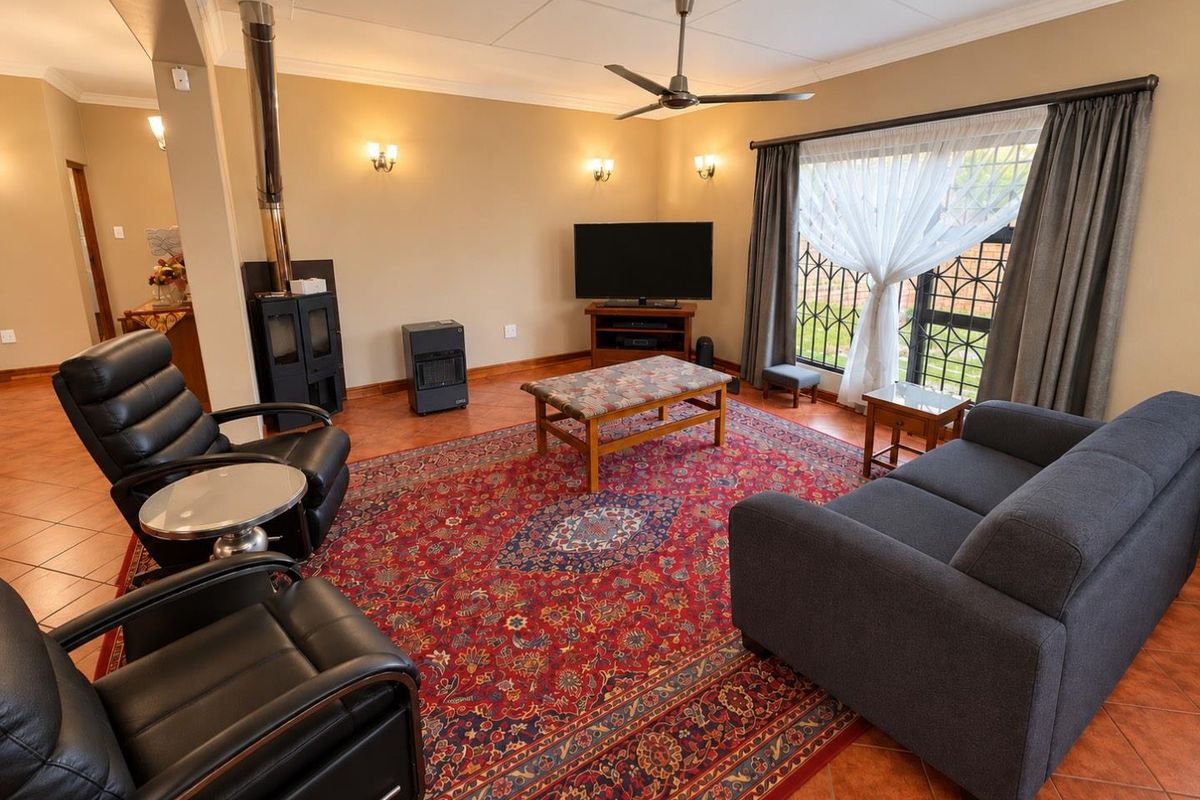 Spacious living room featuring a wood-burning fireplace, ceiling fan, tiled flooring, and large windows with security gates, offering a comfortable and functional living space.