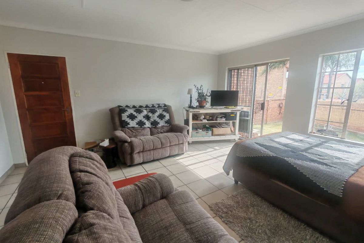A living room featuring tiled flooring, a wooden door, and large windows providing natural light and access to the exterior.