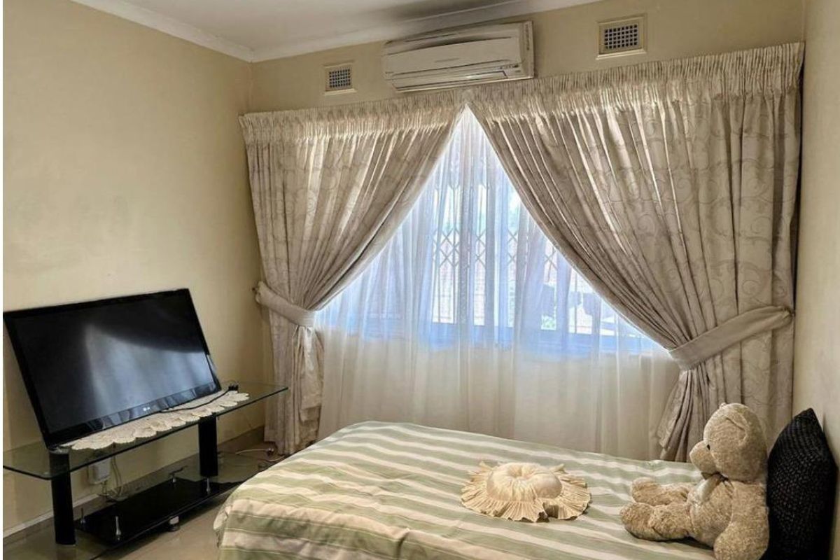A bedroom featuring tiled flooring, a wall-mounted air conditioning unit, and security bars on the window.