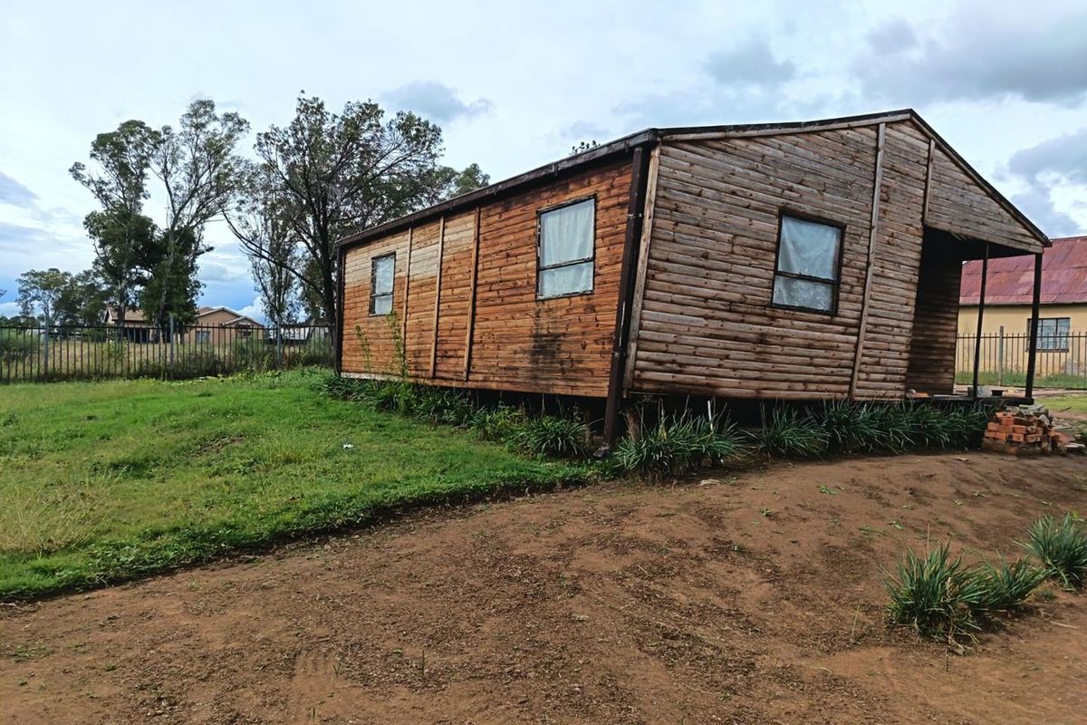 A detached timber-clad structure showing significant structural leaning and signs of weathering, situated on a rural small holding plot.