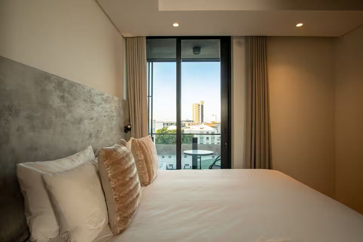 A modern bedroom featuring a textured feature wall, recessed ceiling lighting, and large sliding glass doors opening to a private balcony with city views.