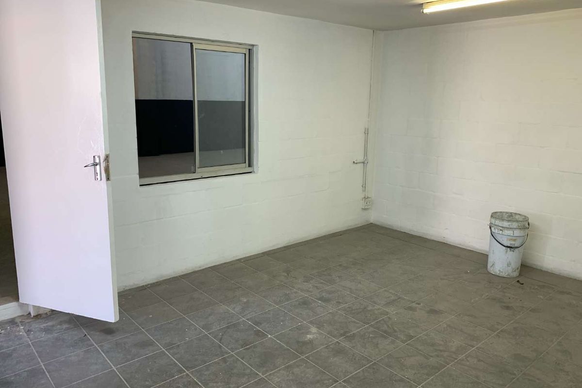 A functional, empty utility space featuring tiled flooring, painted block walls, a sliding window, and overhead fluorescent lighting.