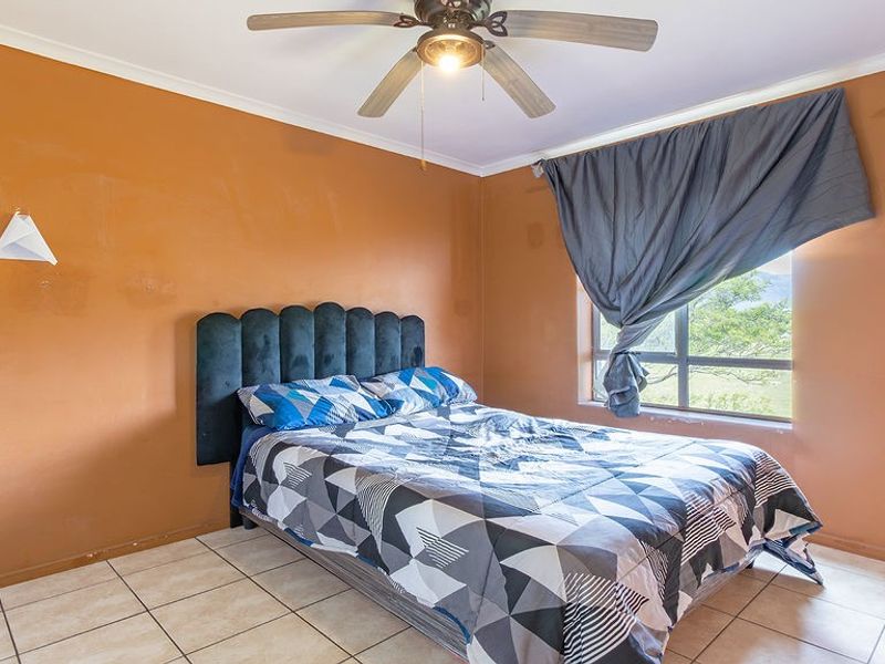 A bedroom featuring tiled flooring, a ceiling fan, and a large window. The room requires cosmetic updates to the wall finishes.