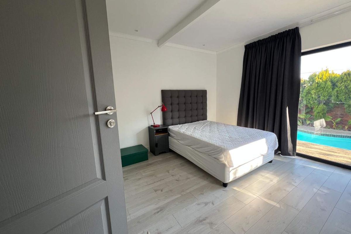 A bright bedroom featuring light wood-look flooring, recessed ceiling lighting, and a large sliding glass door providing direct access to the pool area.