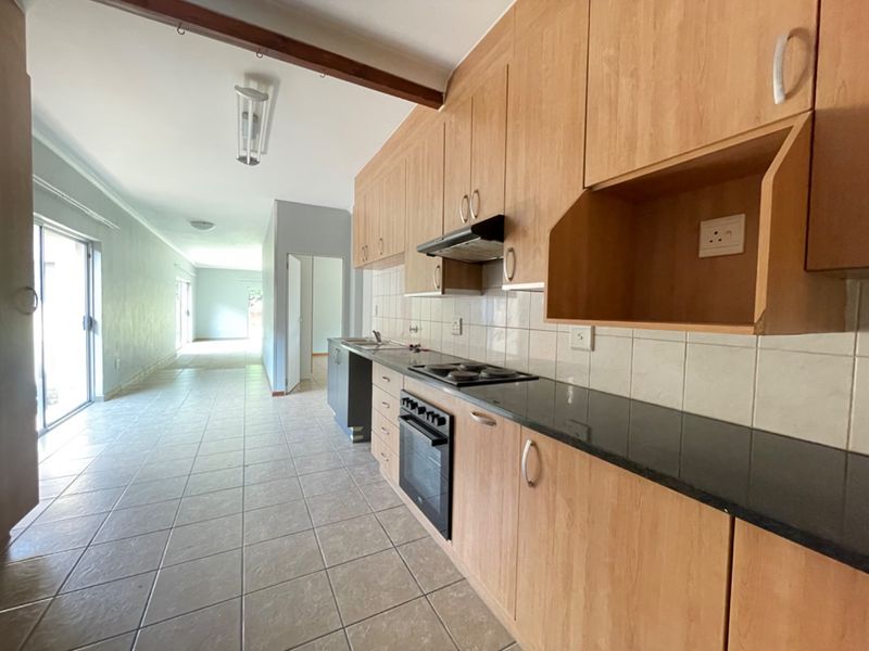 A functional kitchen featuring laminate cabinetry, granite countertops, and built-in appliances, flowing into an open-plan living area with tiled flooring throughout.