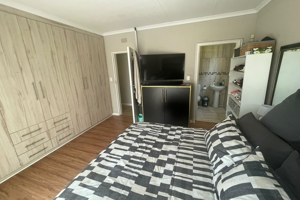 A well-maintained bedroom featuring extensive built-in cupboards, laminate flooring, and direct access to an en-suite bathroom.