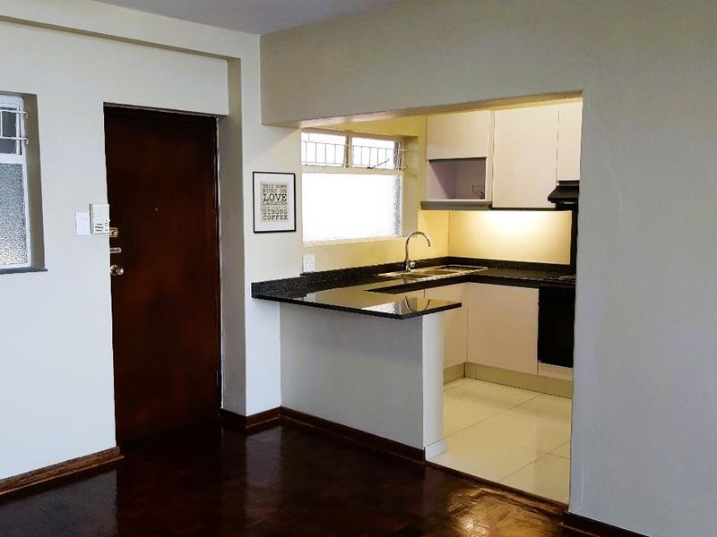 Open plan living area featuring a compact kitchen with granite countertops, built-in cabinetry, and integrated appliances, adjacent to a hardwood floored living space.