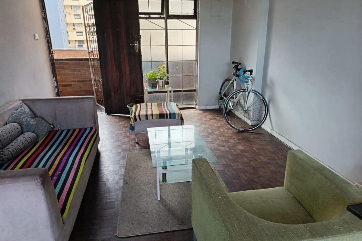 A living room area featuring parquet flooring and access to an external balcony through a security gate and sliding door.