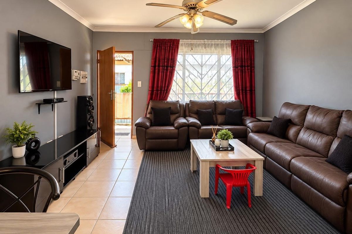 A well-maintained living room featuring tiled flooring, a ceiling fan, and direct access to an outdoor area through a secure door.