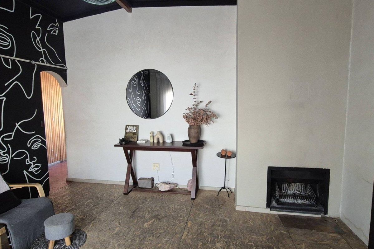 Living room featuring a built-in fireplace, exposed ceiling beams, and a distinctive mural wall, offering a unique character space.