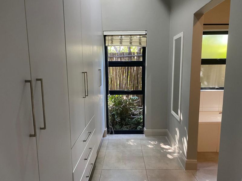 A bright hallway featuring extensive built-in cabinetry, neutral tiled flooring, and a window providing natural light and garden views.