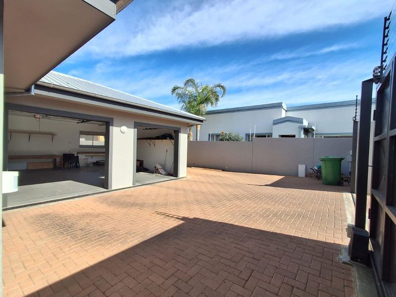 A paved rear courtyard area featuring a detached garage structure, secure boundary walls with electric fencing, and a metal gate entrance.