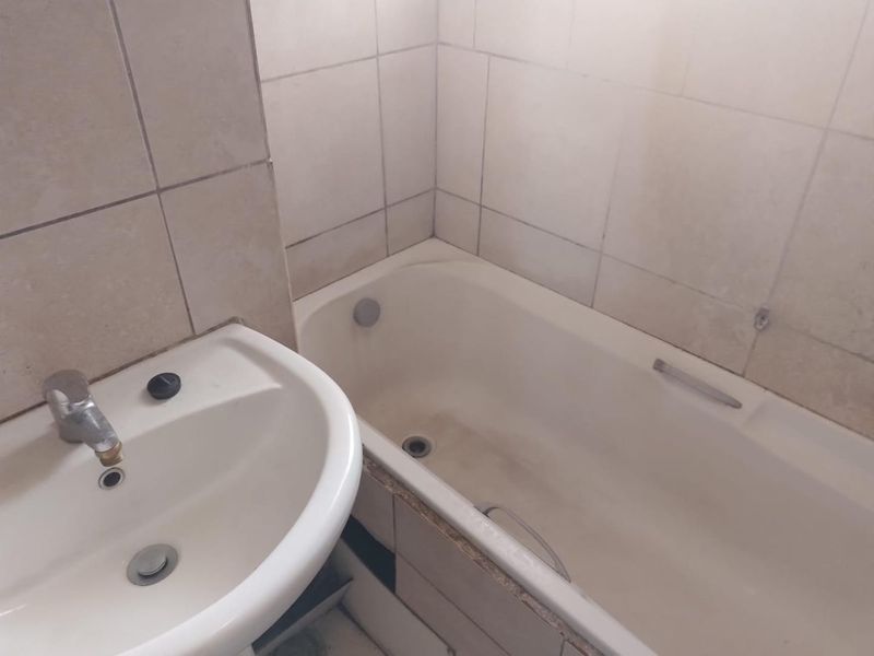 A functional bathroom featuring a bathtub and washbasin with tiled walls, currently showing signs of wear and requiring maintenance.