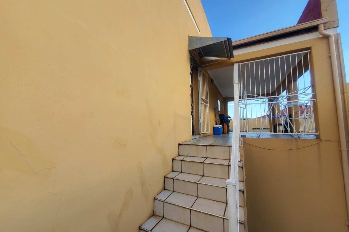 Exterior view of an apartment entrance featuring tiled stairs leading to a covered patio area with metal security railings.
