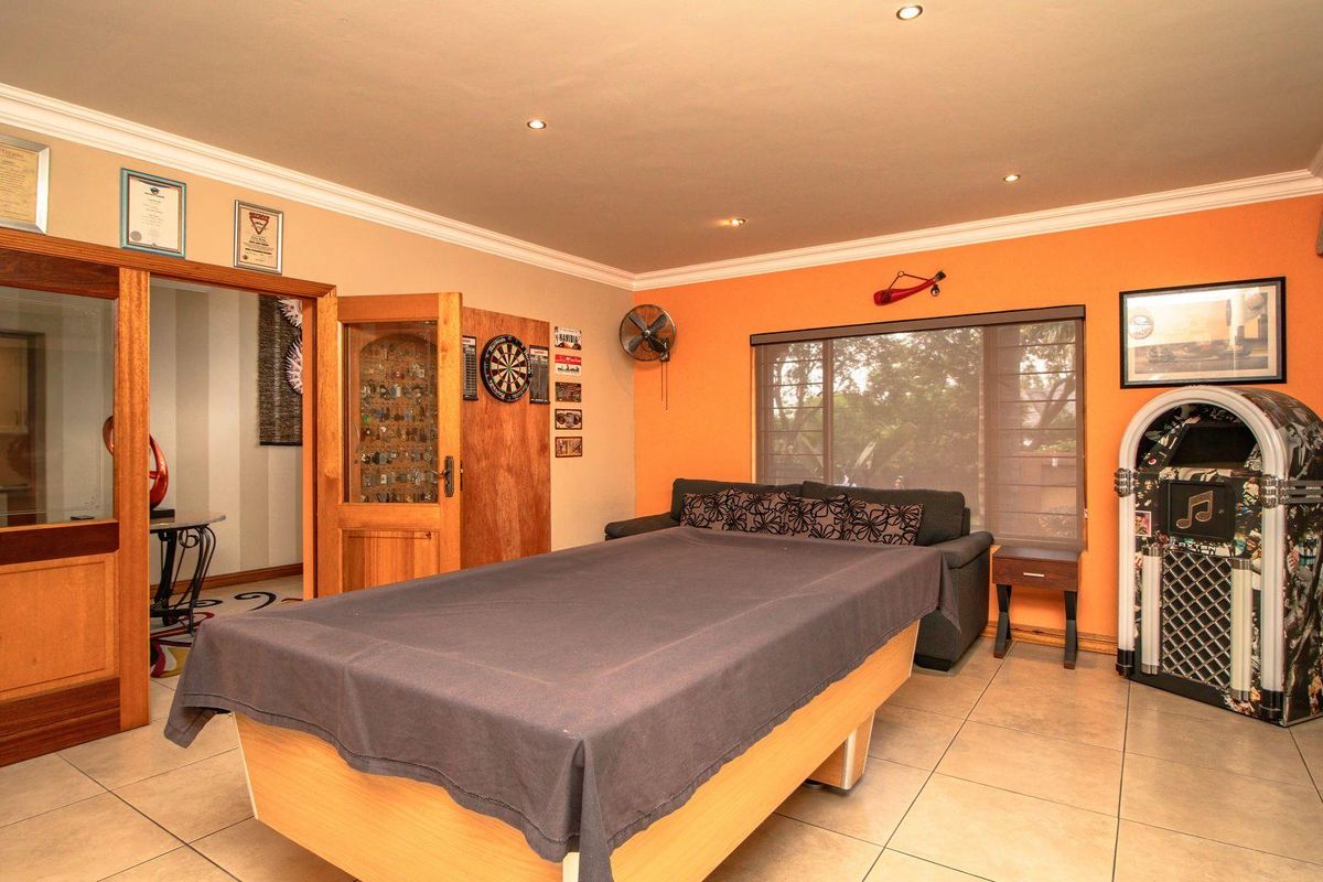 A spacious entertainment room featuring tiled flooring, recessed ceiling lighting, and wooden door frames, currently set up as a games room.