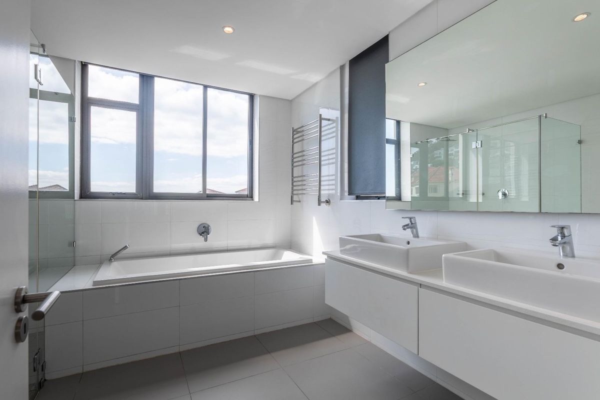 Modern, bright bathroom featuring a double vanity, built-in bathtub, large wall mirror, and a heated towel rail with clean, contemporary finishes.