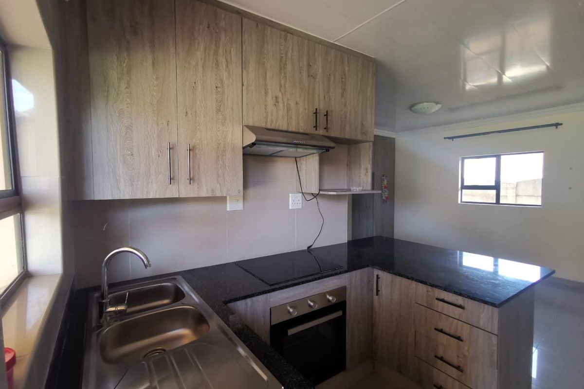 Modern kitchen featuring wood-look laminate cabinetry, granite countertops, built-in oven, electric hob, and a stainless steel double sink.