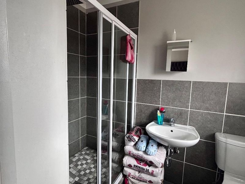 A functional bathroom featuring a shower enclosure, wall-mounted basin, and toilet with grey tiled wall finishes.