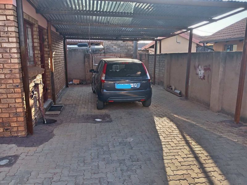 A covered carport area featuring paved flooring and brick boundary walls, providing secure off-street parking.