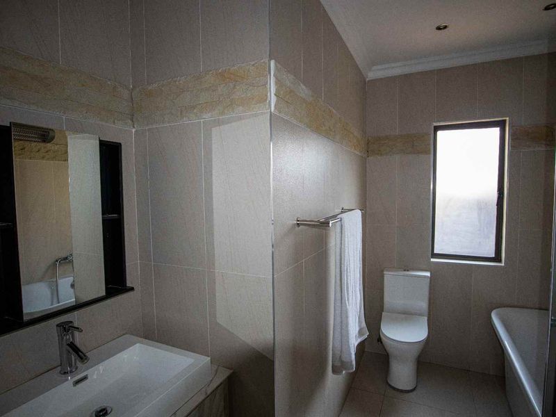 A modern bathroom featuring tiled walls, a vanity basin, a toilet, and a bathtub, complemented by recessed lighting and a window for natural light.