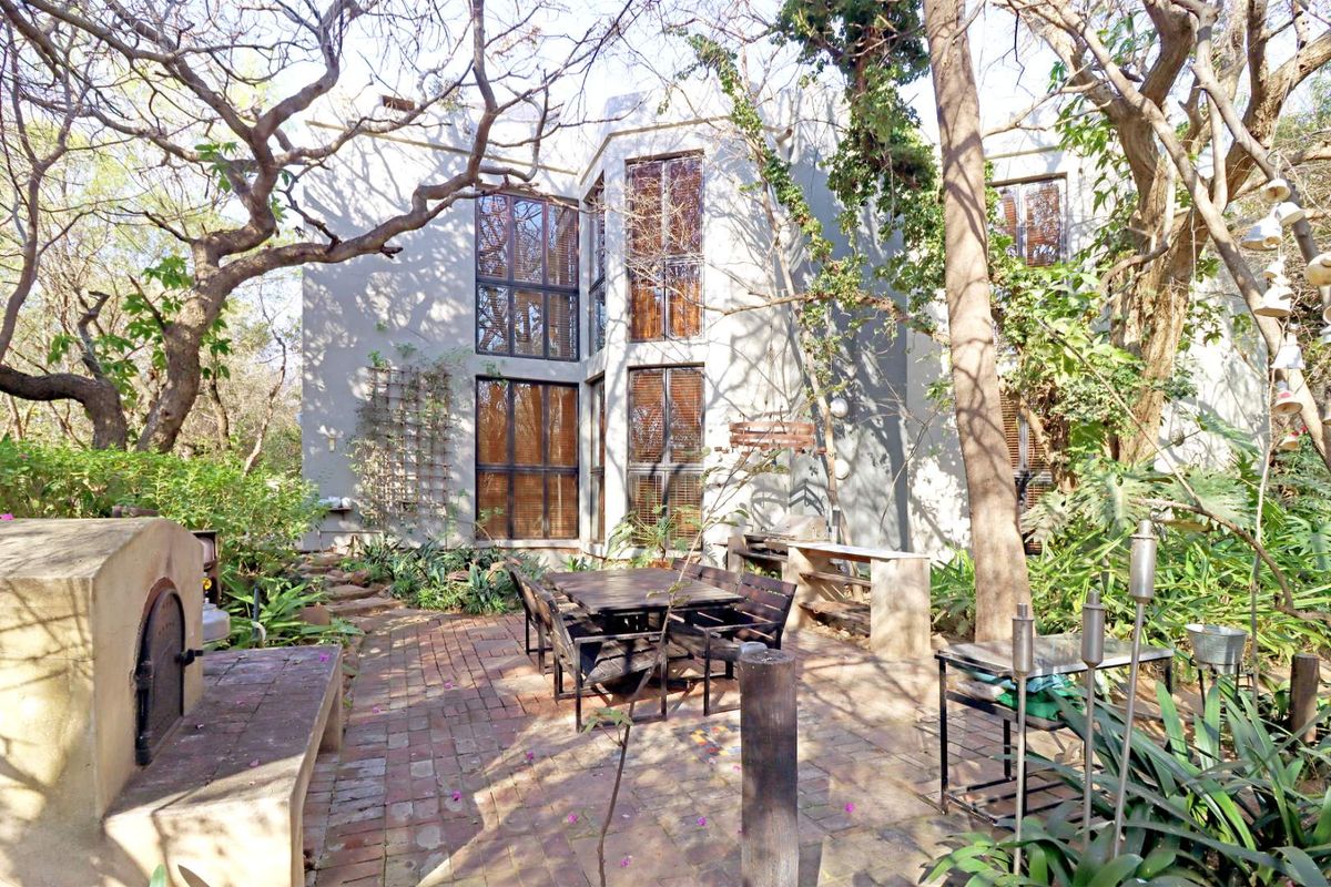 A tranquil rear garden patio featuring a brick-paved entertainment area with a built-in pizza oven and braai, set against a multi-story residential facade.