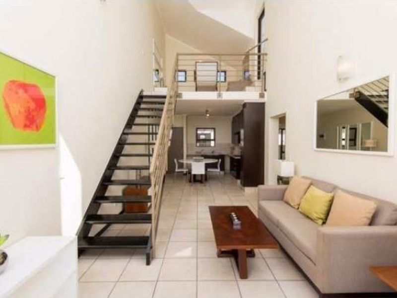 Open-plan living area featuring a modern staircase leading to a mezzanine level, tiled flooring, and a functional kitchen space.