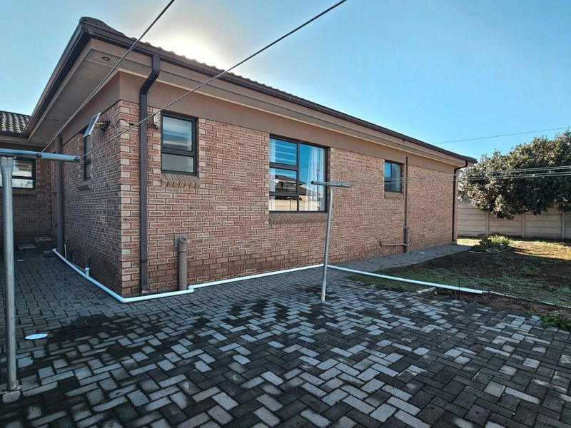 Rear view of the property featuring a face brick facade, paved patio area, and established garden space.