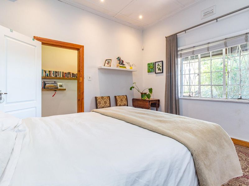 A bedroom featuring a window with security bars, recessed downlighting, and an adjoining walk-in closet or storage area with built-in shelving.