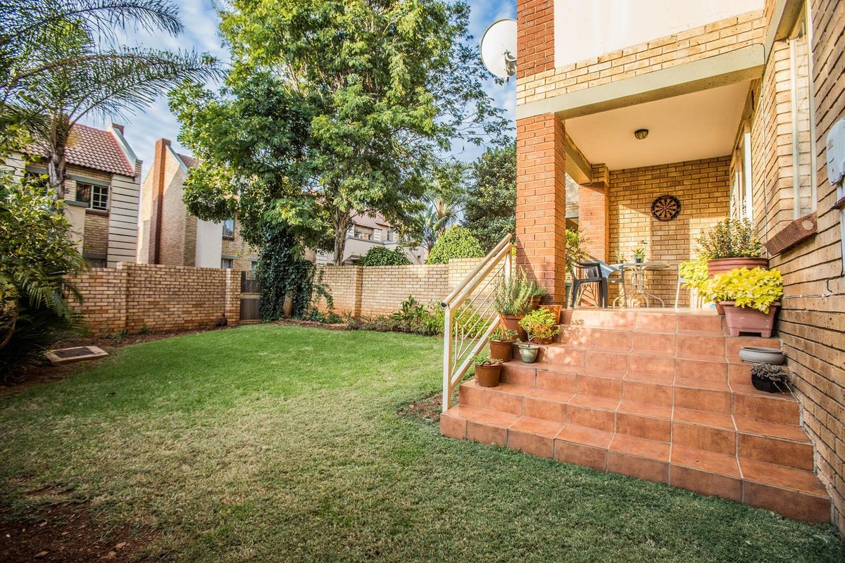 A private rear garden featuring a brick boundary wall, a covered patio with tiled steps, and a well-maintained lawn area.