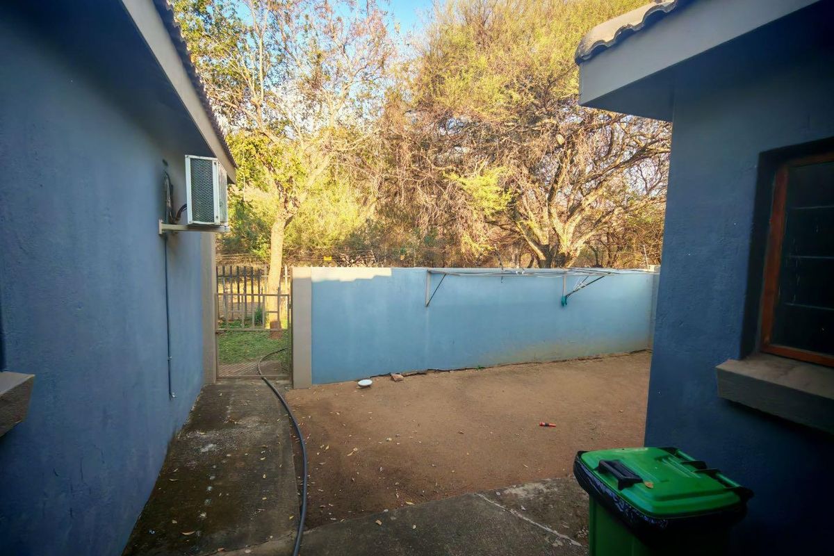A rear courtyard area featuring concrete paving, a boundary wall, and an external air conditioning unit mounted on the side of the house.