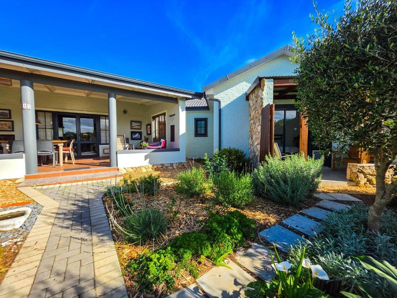 A well-maintained rear exterior featuring a covered patio, stone-accented brick facade, and a landscaped garden with paved pathways.