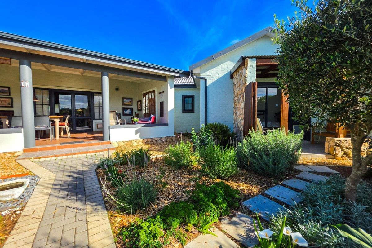 A well-maintained rear exterior featuring a covered patio, stone-accented brick facade, and a landscaped garden with paved pathways.