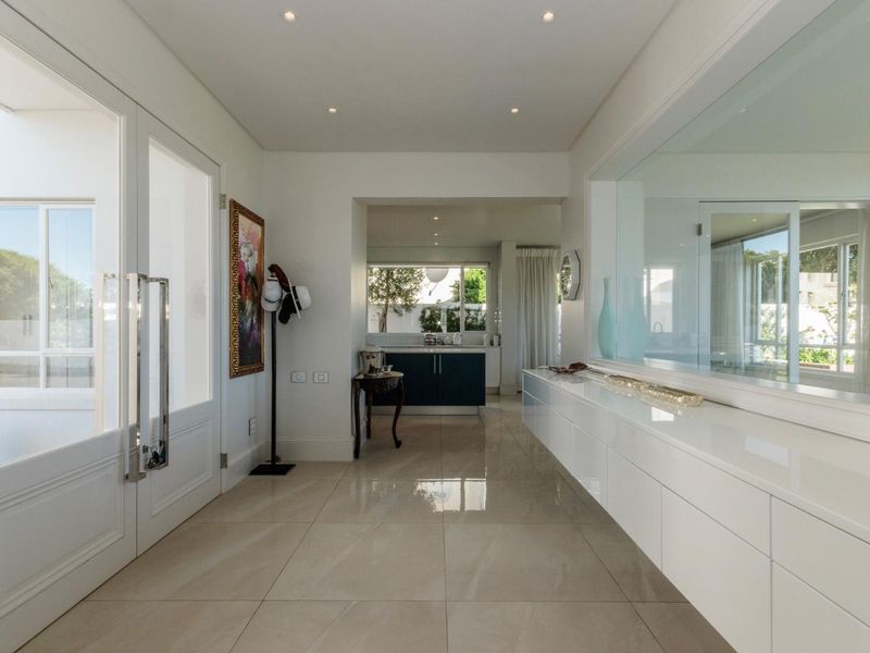 Bright and modern entrance hall featuring polished tiled flooring, recessed lighting, and sleek built-in cabinetry with a large internal window looking through to the kitchen.