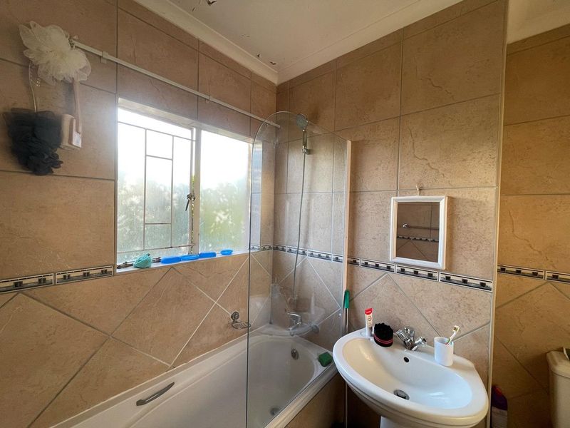 A functional bathroom featuring a bathtub with a glass shower screen, pedestal basin, and neutral ceramic wall tiling.