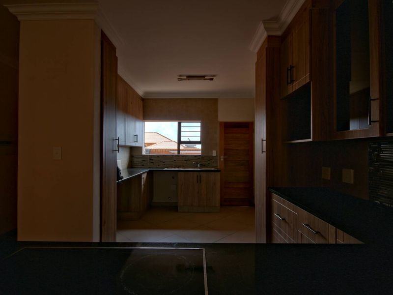 A functional kitchen featuring wood-finish cabinetry, dark stone countertops, and tiled flooring, offering a clean and practical layout for meal preparation.