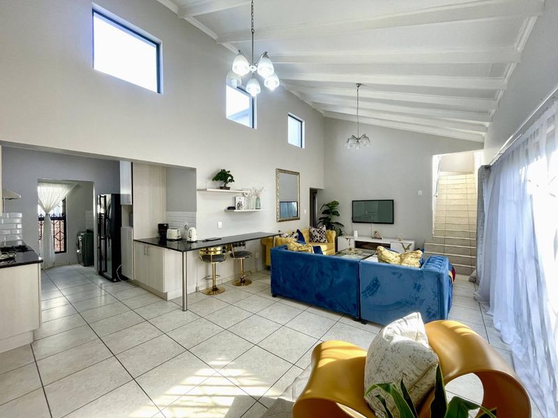 Spacious open-plan living area featuring vaulted ceilings with exposed beams, tiled flooring, a breakfast bar, and a staircase leading to the upper level.