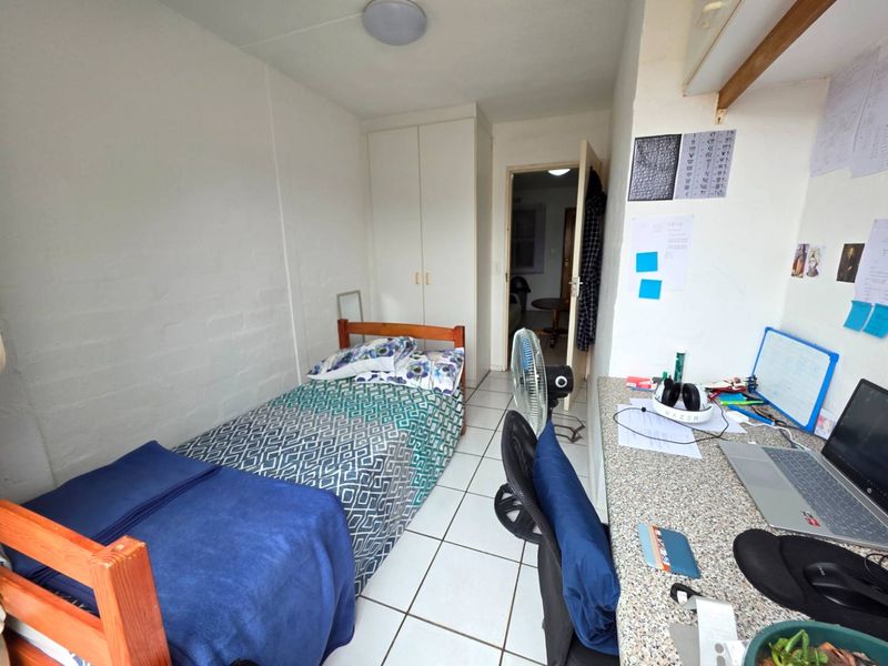 A compact bedroom featuring tiled flooring, a built-in wardrobe, and a fixed desk area, offering a functional space for study or rest.