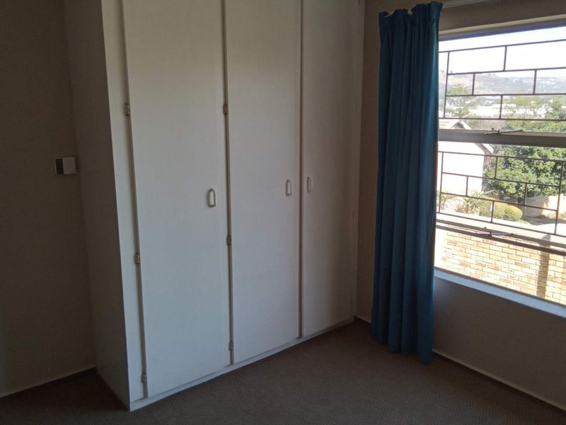 A vacant bedroom featuring built-in cupboards, carpeted flooring, and a window fitted with security bars.