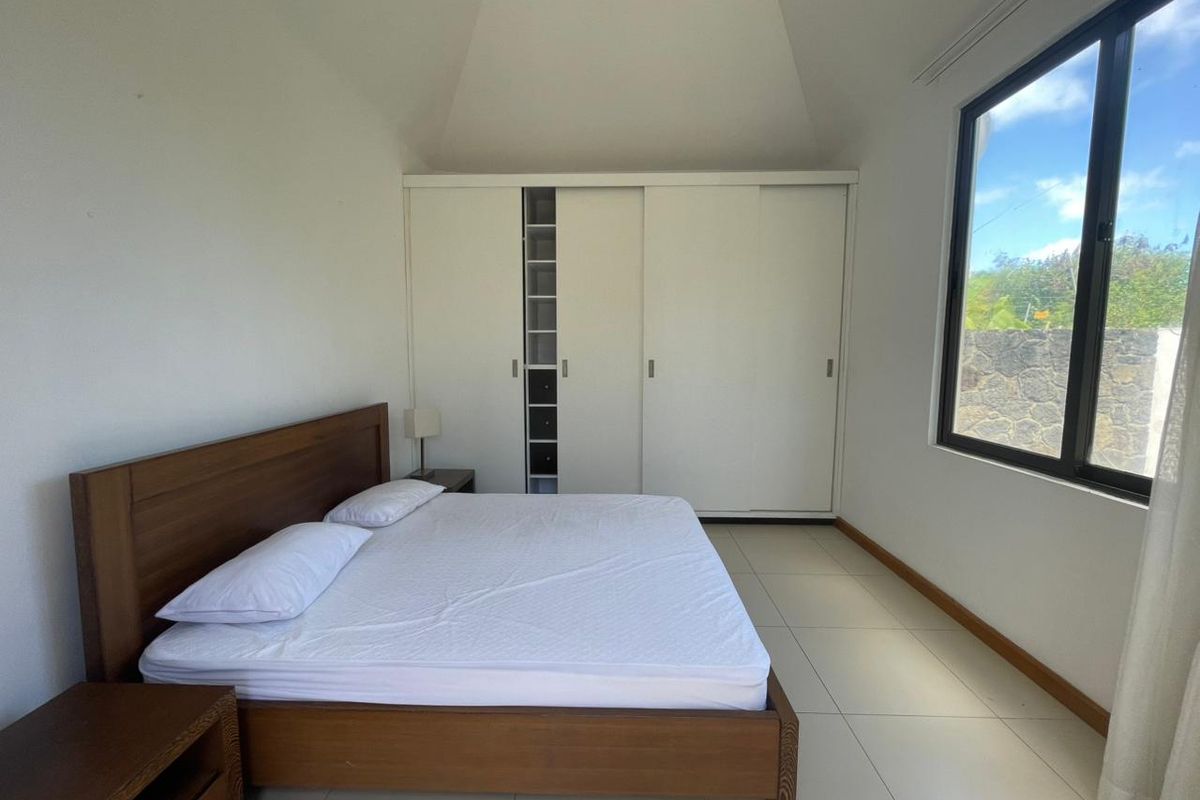 A bright bedroom featuring high vaulted ceilings, large format floor tiles, and a built-in sliding door wardrobe.