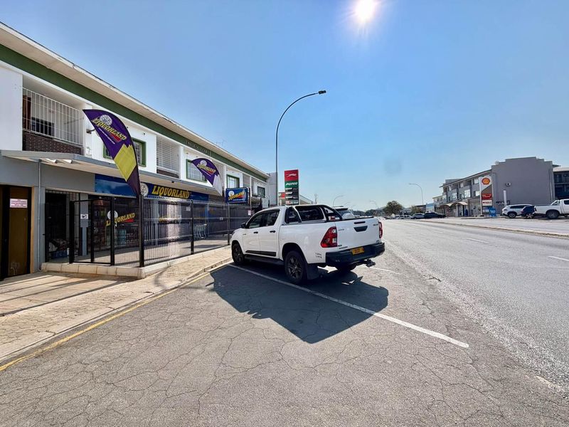 Street-level view of a commercial property featuring a storefront with security gates and adjacent paved parking area.