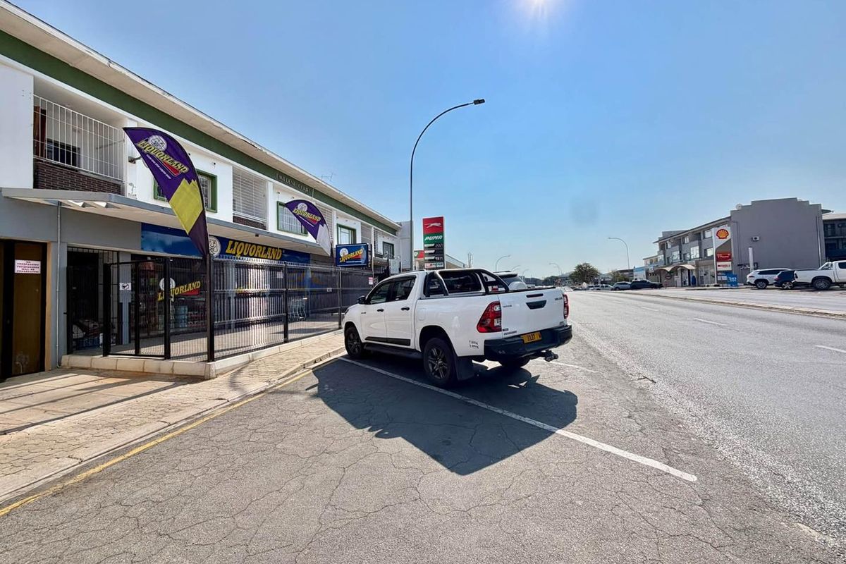 Street-level view of a commercial property featuring a storefront with security gates and adjacent paved parking area.