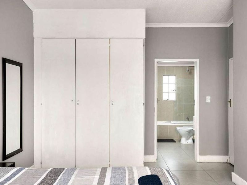 A bedroom featuring built-in cupboards and tiled flooring, with direct access to an adjoining en-suite bathroom.