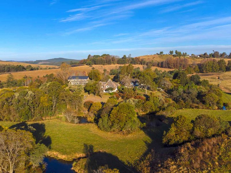 An aerial view of the guest house property set within a sprawling rural landscape featuring mature trees and natural water features.