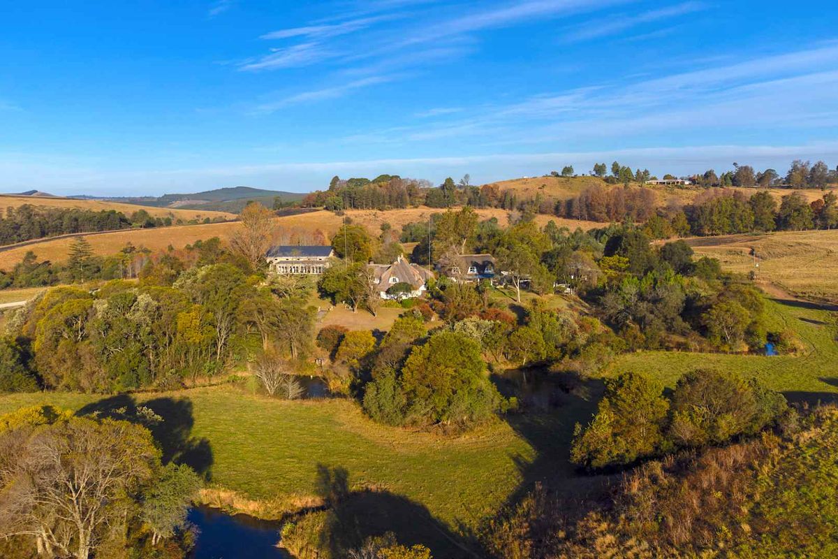 An aerial view of the guest house property set within a sprawling rural landscape featuring mature trees and natural water features.