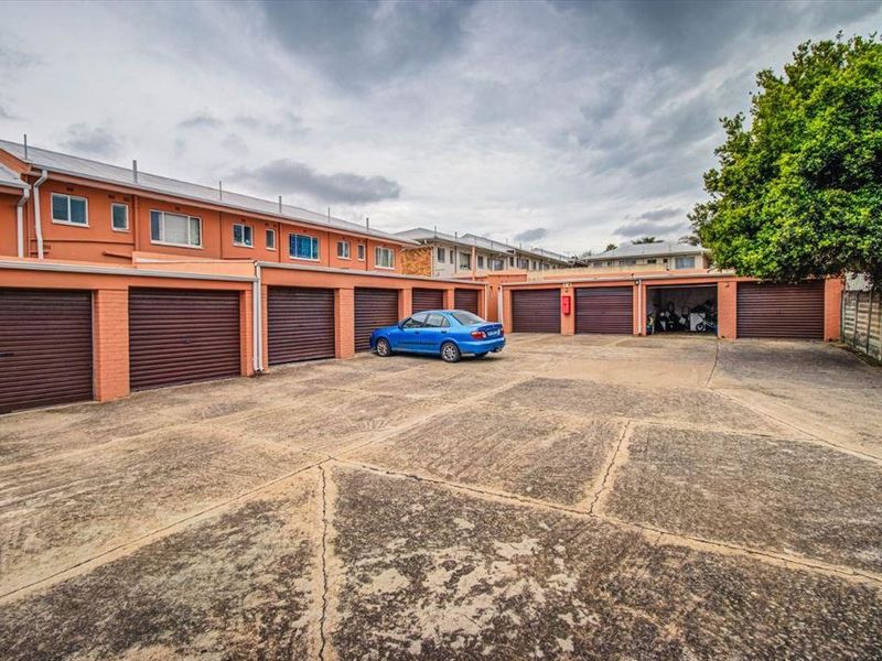 A row of residential garages with roller shutter doors and a shared concrete driveway area.