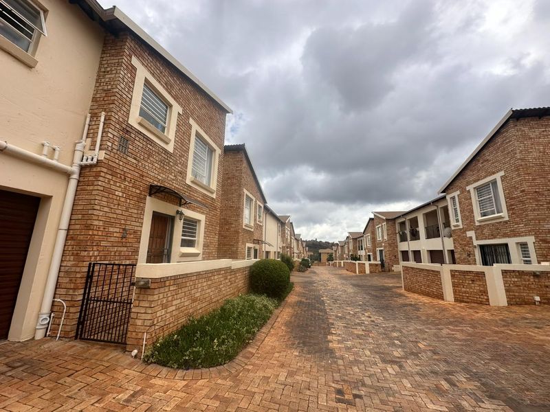 A view of a townhouse complex featuring face-brick facades, paved driveways, and secure boundary walls under an overcast sky.