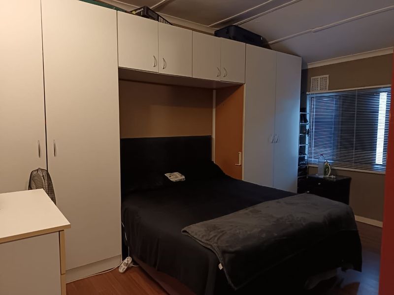 A bedroom featuring extensive built-in white cabinetry surrounding the bed area, laminate flooring, and a window with fitted venetian blinds.